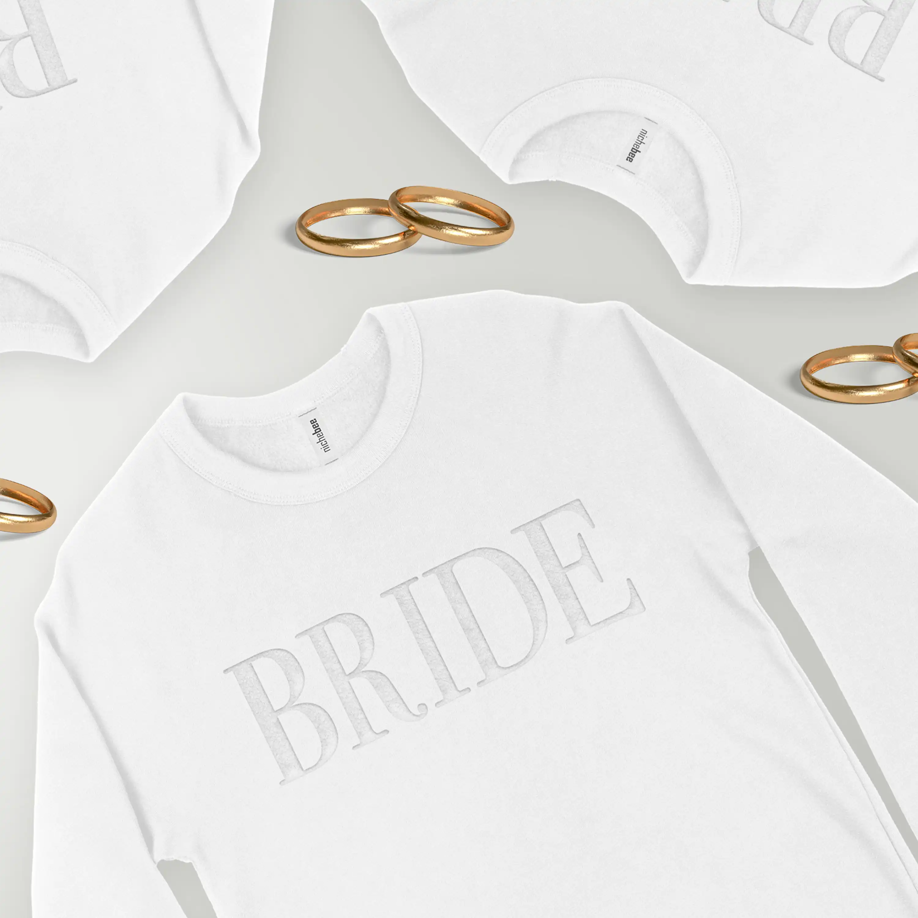 White sweatshirt with 'BRIDE' text on a light gray background with gold rings.