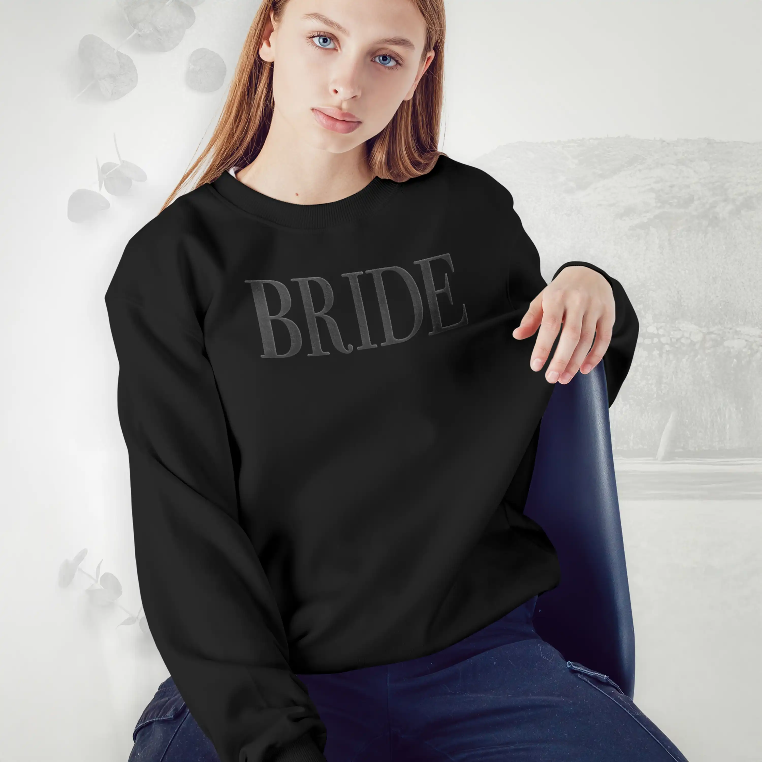 Person wearing a black sweatshirt with 'BRIDE' text, sitting on a chair against a light gray background.