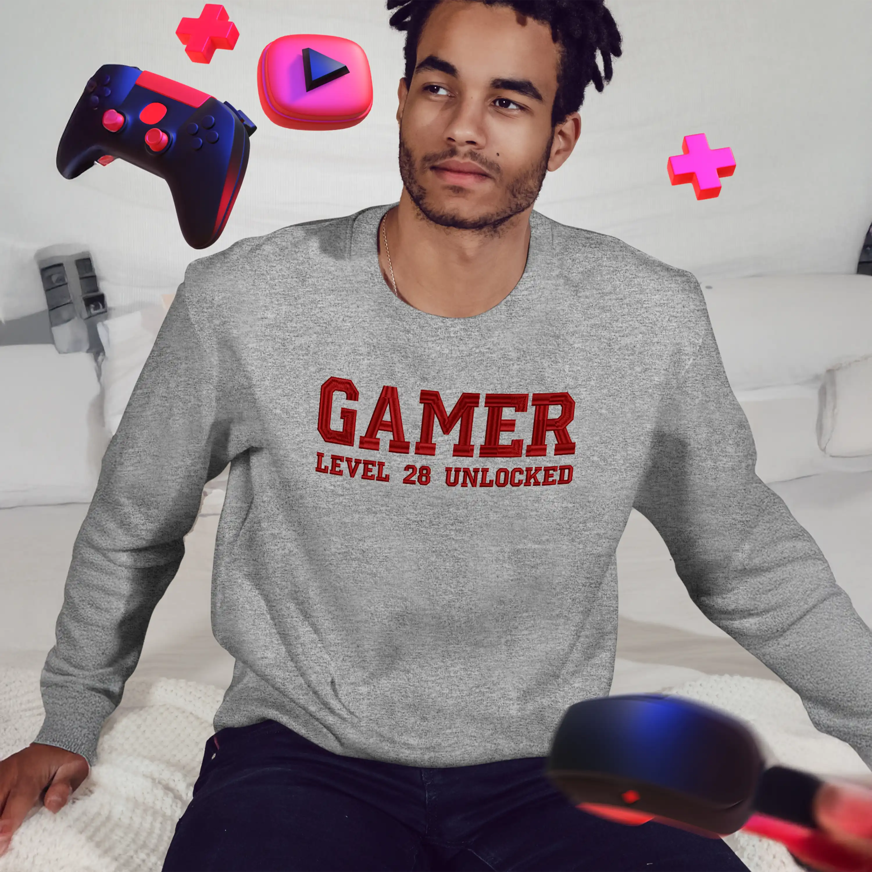 Person wearing a gray sweatshirt with 'Gamer Level 28 Unlocked' text, sitting on a couch with gaming controllers.