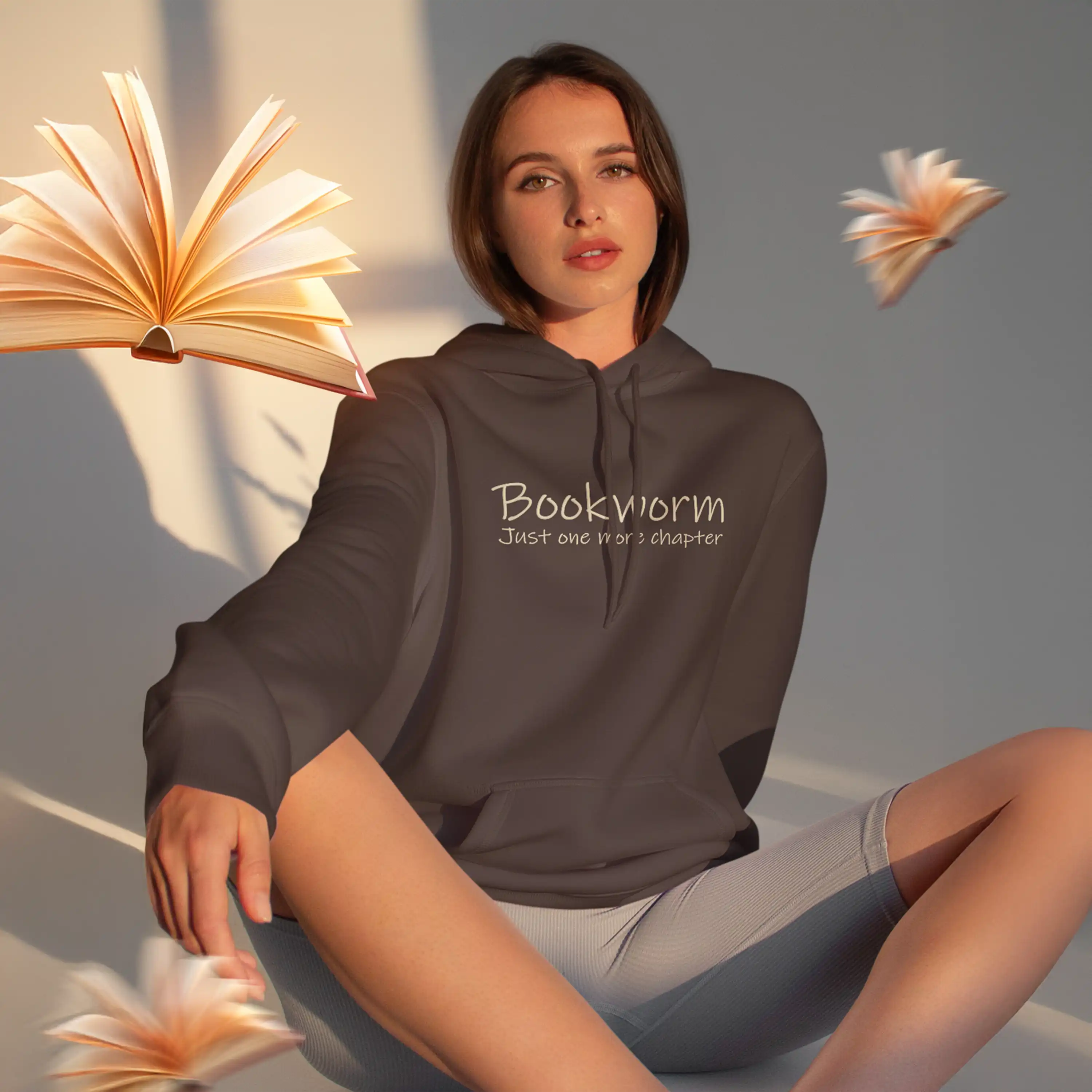 Woman wearing a hoodie with 'Bookworm Just One More Chapter' text, surrounded by book-shaped flowers.